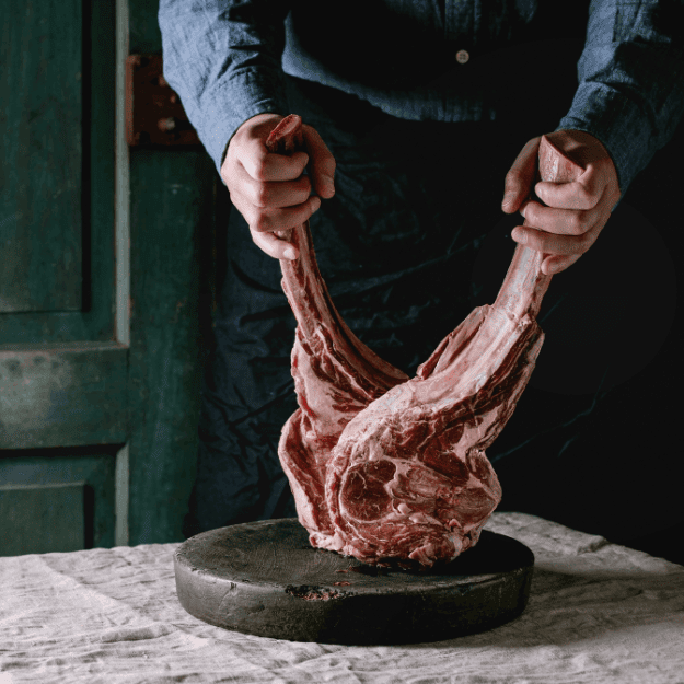 A man holding 2 large bone-in steaks