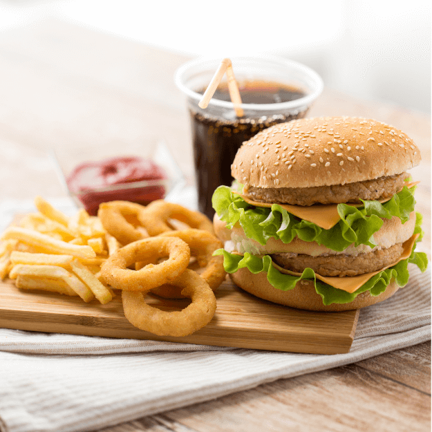 A burger, fries, onion rings, ketchup and soda depicting processed food